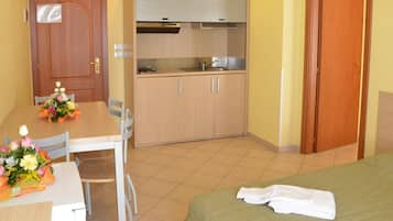 Una camera d'albergo compatta con un letto, una scrivania piccola con una sedia, un angolo cottura e una porta in legno.