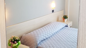 Ein Schlafzimmer mit einem Bett, einem Nachttisch, einem Spiegel und einer Wandleuchte.