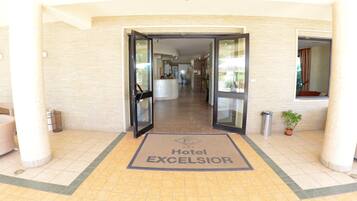 Entrada de un hotel con mostrador de recepción, zona de espera con sillas y suelo de baldosas.