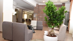 Eine Lobby mit grauen Sofas, einem Topfpflanzen und einer Rezeption.