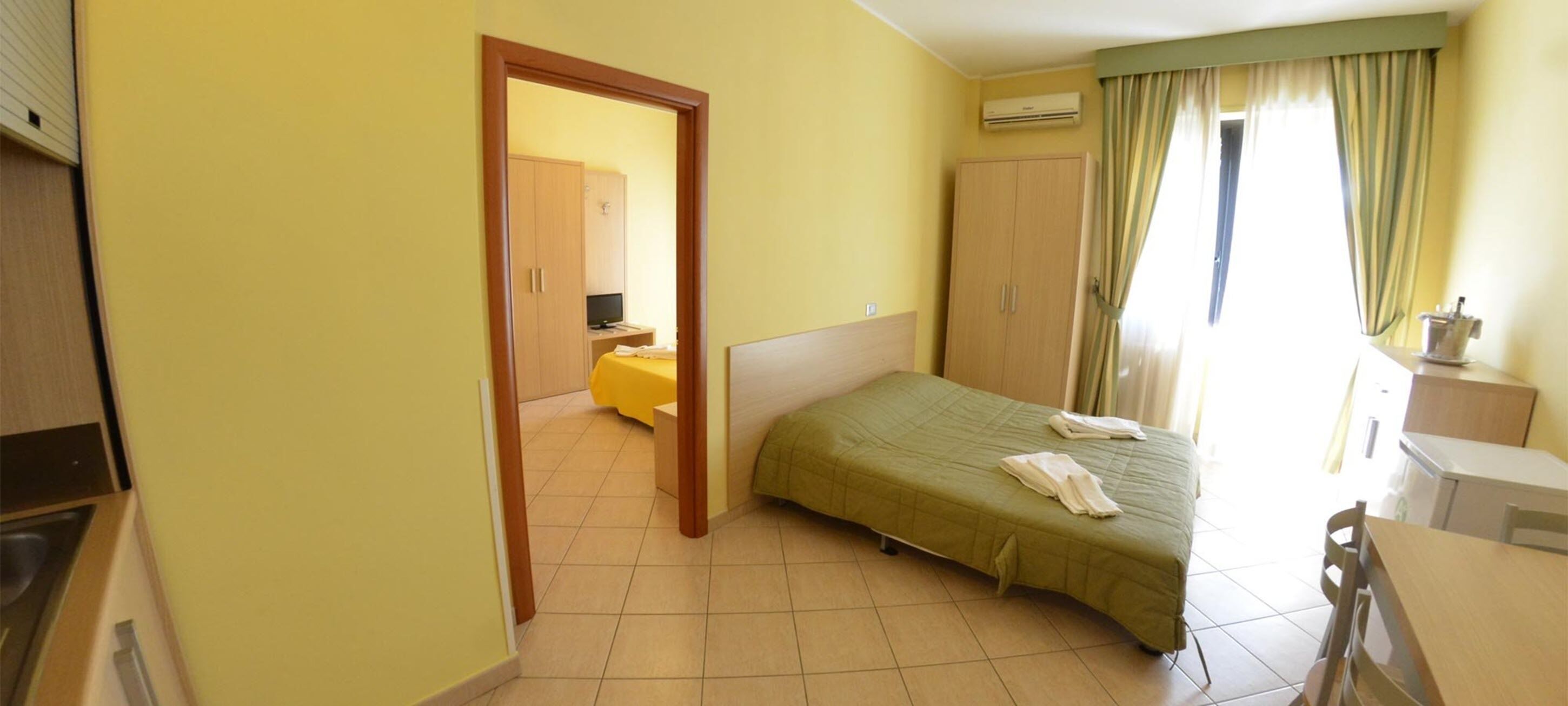 Quarto de hotel com cama, escrivaninha, cadeira, guarda-roupa e ar condicionado.