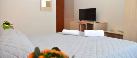 Habitación de hotel con cama, escritorio con televisor, espejo y una planta pequeña en maceta.