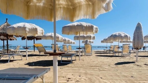 Ein Strand mit Reetsonnenschirmen und Liegestühlen.