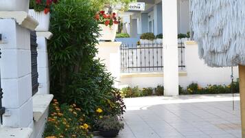 A hotel entrance with a sign reading "RESIDENCE HOTEL EXCELSIOR" and a pathway lined with flowers.