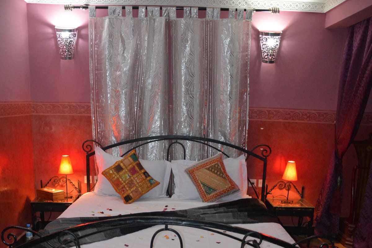 A bed with a metal frame, two bedside tables with lamps, a patterned rug, and a decorative table in front of the bed.