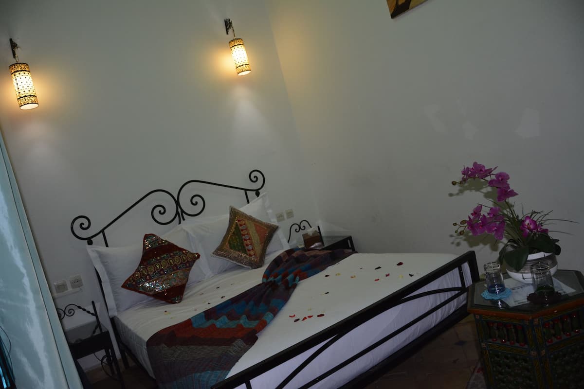 A bed with a metal frame, decorative pillows, a patterned blanket, and a vase with flowers on a side table.