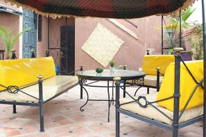 Un patio con sillas amarillas acolchadas y una mesa redonda, un tapete tejido en la pared y una puerta azul.