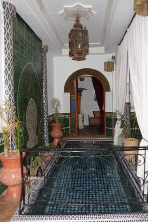 A traditional Moroccan interior with a tiled floor, a decorative lantern, and a view into a room with a bed and curtains. - Riad Assalam (Marrakech)