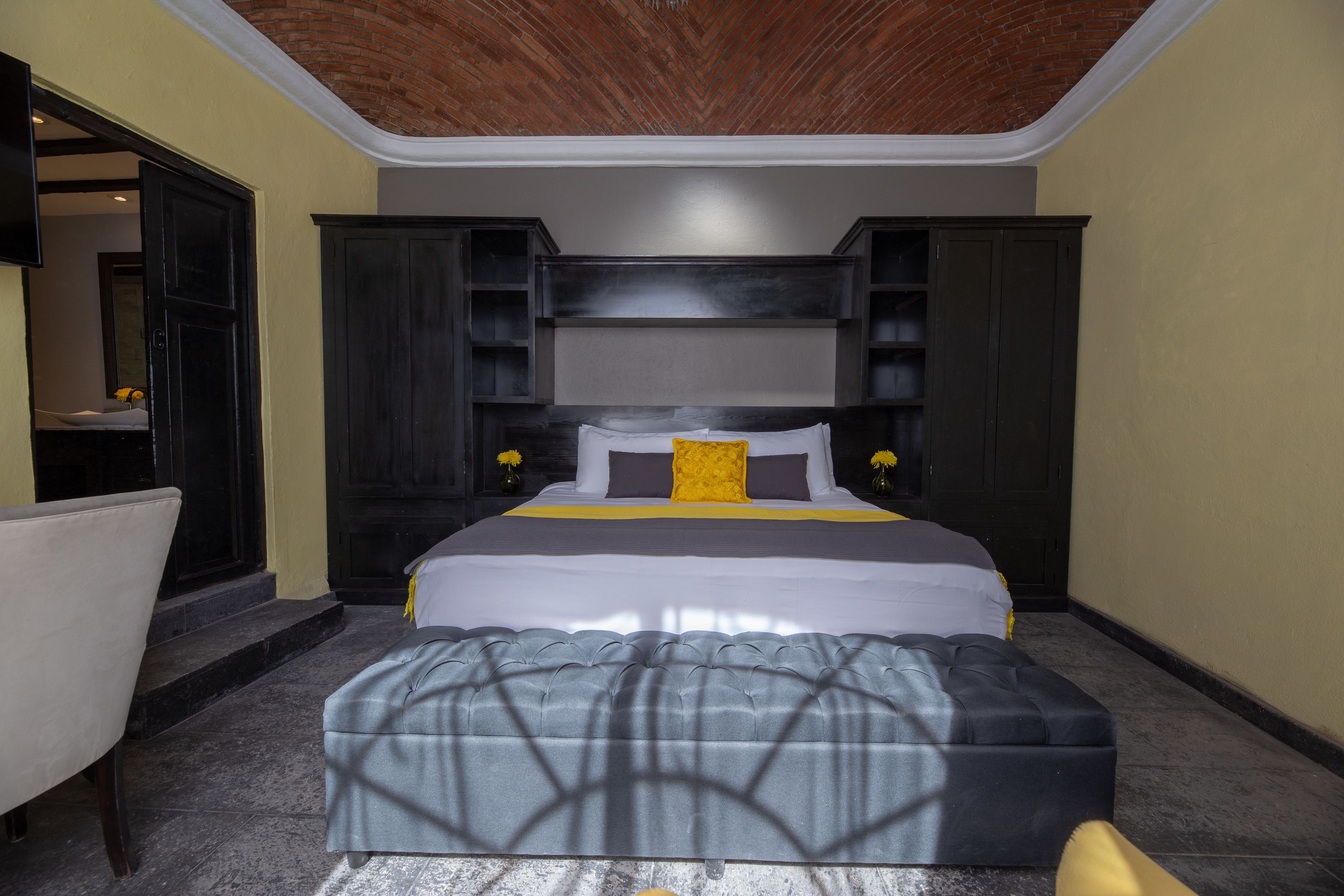 A bedroom with a large bed, dark wooden headboard, and a grey upholstered bench.