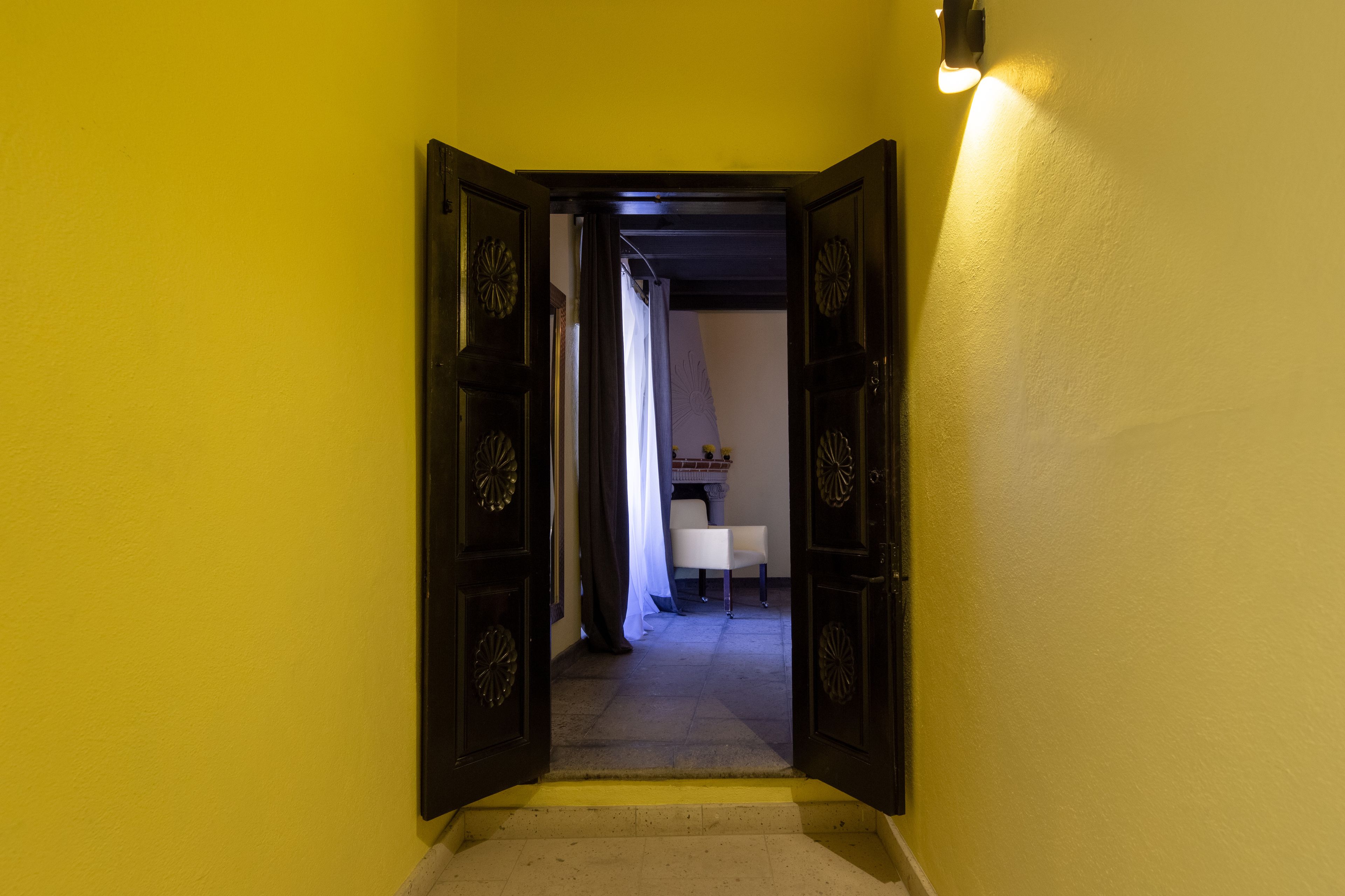 A hallway with a yellow wall, a white chair, and a door leading to another room.