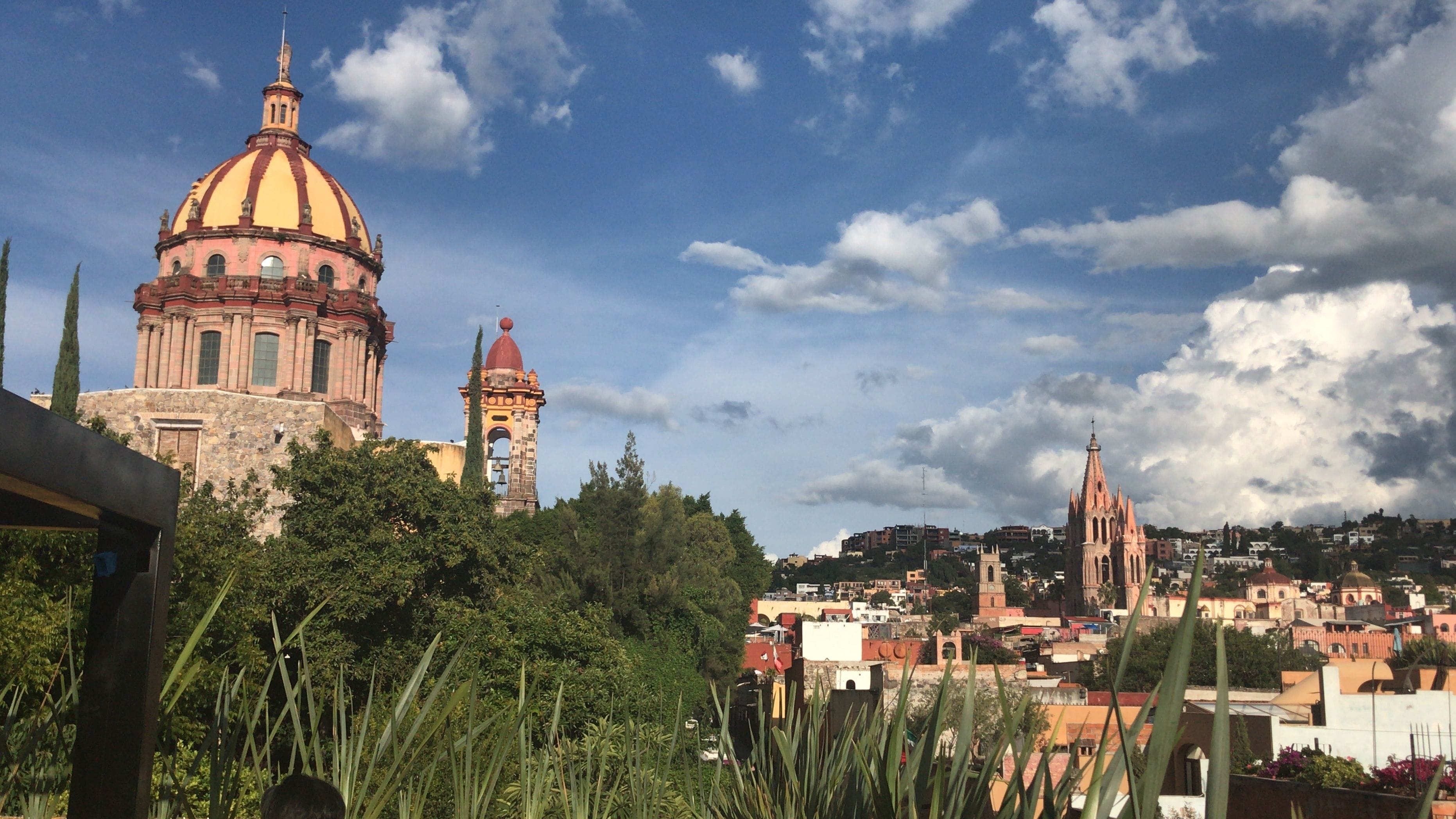 A historic building with a prominent dome and bell tower, surrounded by lush greenery and a clear sky.