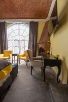 Una habitación con chimenea de ladrillo, sillas amarillas, una mesa negra y una cama con manta amarilla.