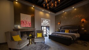 A modern bedroom with a fireplace, a large bed, and a seating area with two armchairs. - Villa Limon Hotel Boutique (San Miguel de Allende)