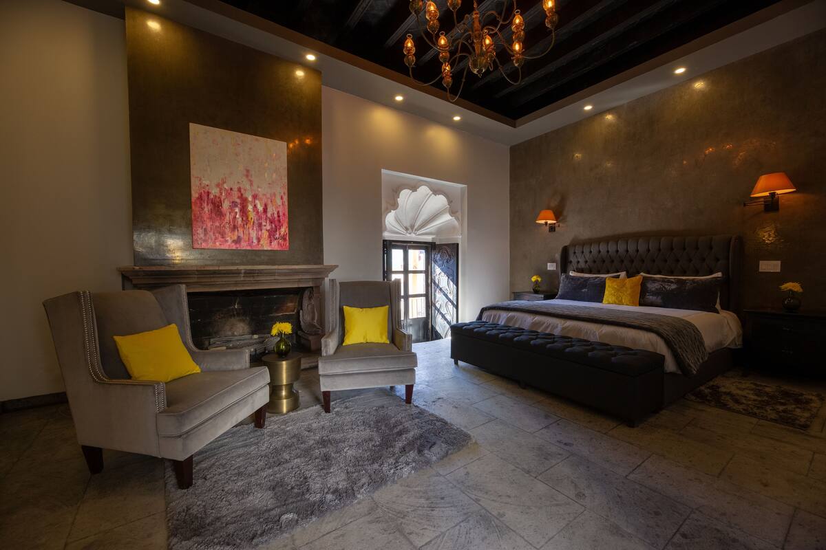Une chambre moderne avec une cheminée, un grand lit et un coin salon comprenant deux fauteuils.
