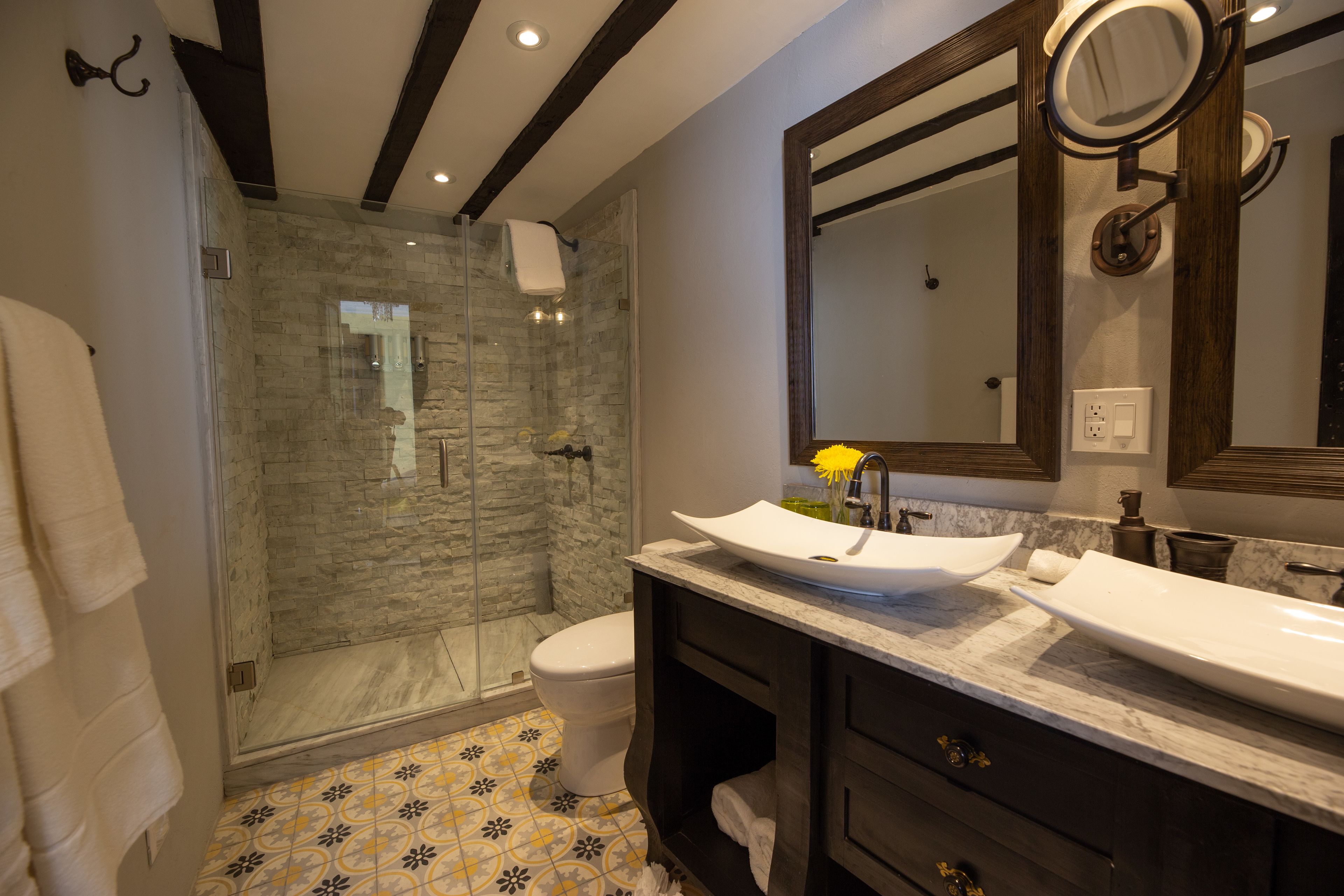 Een moderne badkamer met een douche met glazen wand, twee wastafels en een grote spiegel.