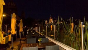 An outdoor dining area with tables and chairs, umbrellas, and a view of a cityscape at night. - Villa Limon Hotel Boutique (San Miguel de Allende)