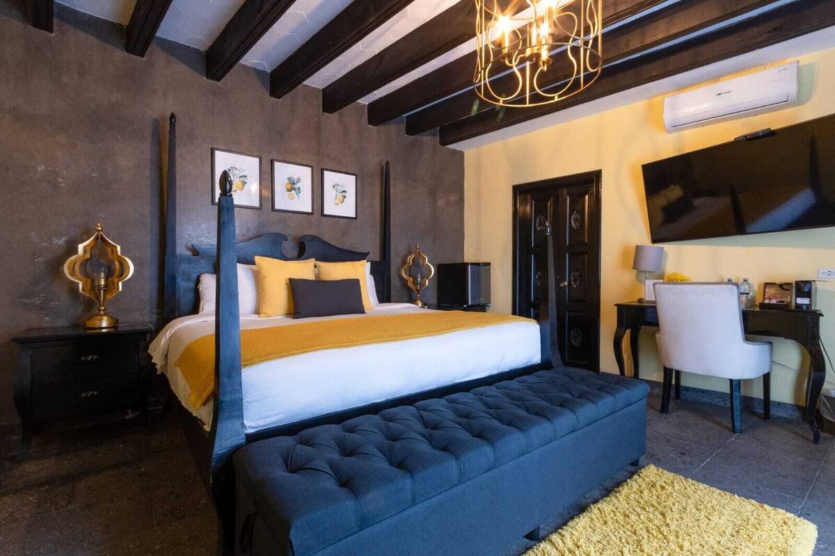 Une chambre à coucher avec un lit à baldaquin, un bureau avec une chaise, une télévision et des œuvres d’art accrochées au mur.