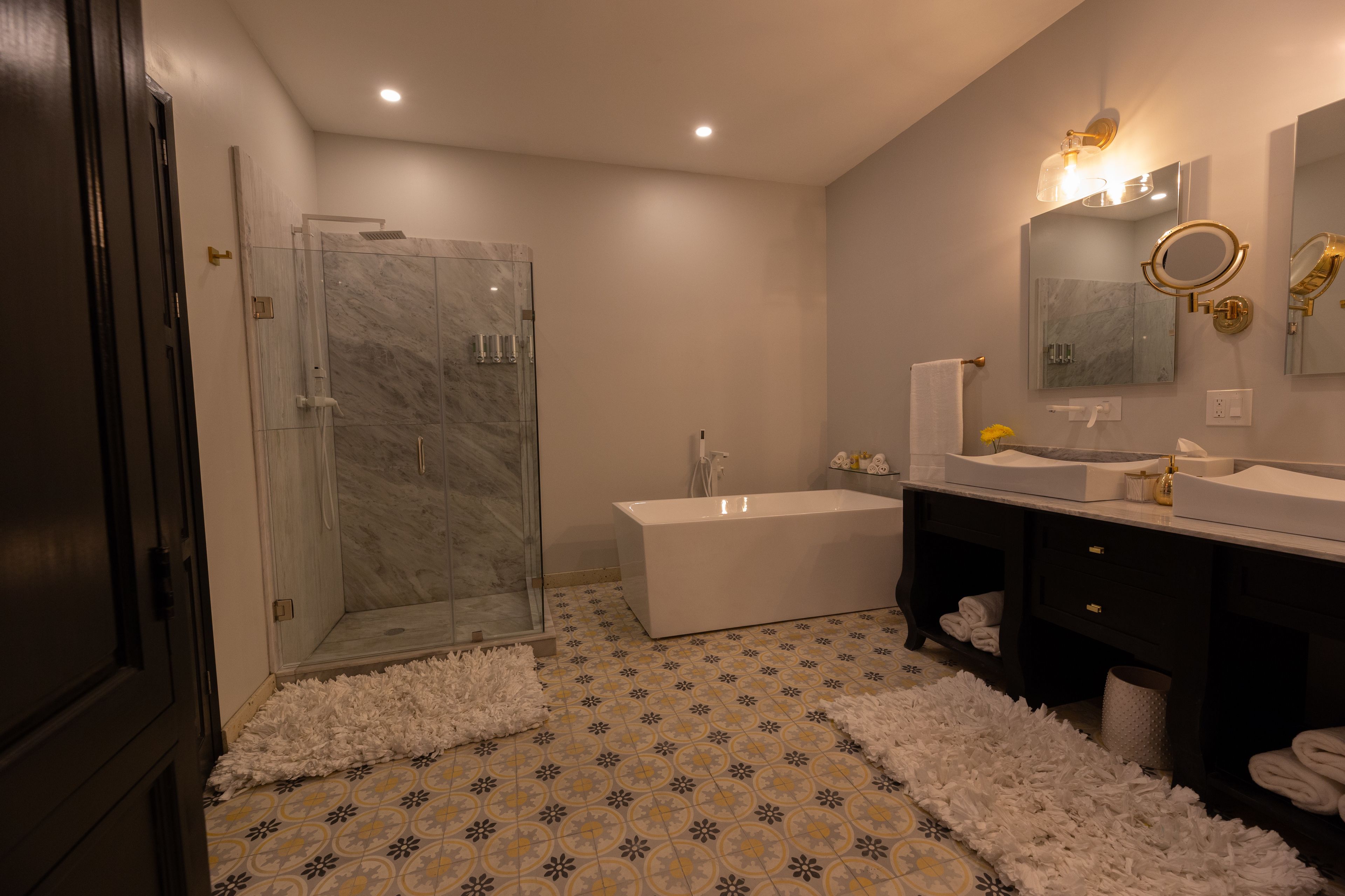 Un baño moderno con cabina de ducha de vidrio, una bañera independiente y un tocador con espejo e iluminación.