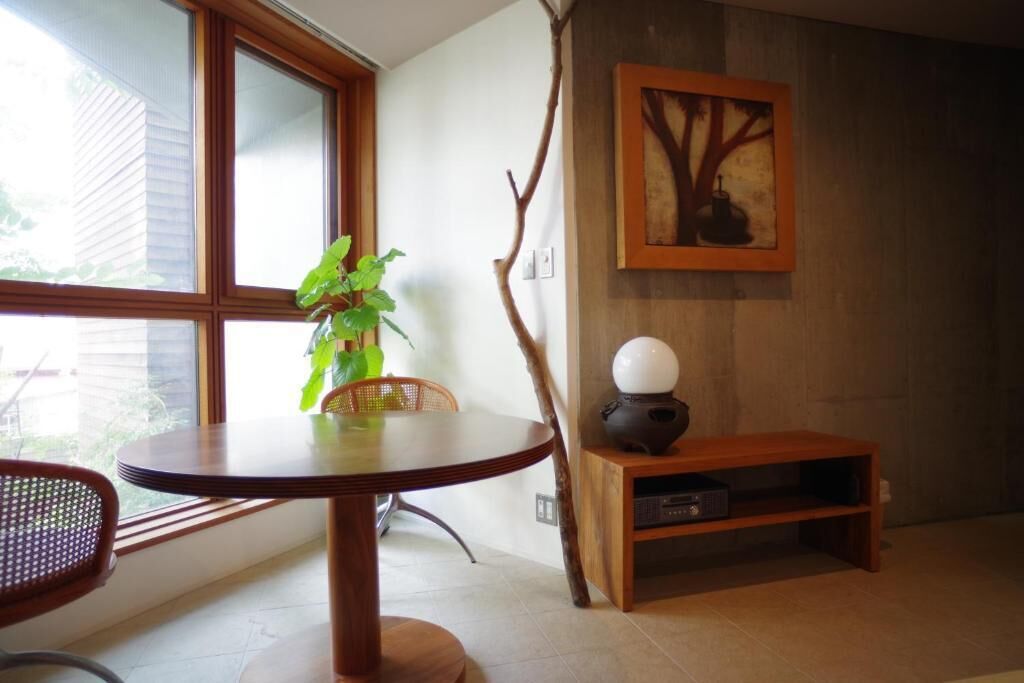 Uma área de jantar com uma mesa redonda, cadeiras, um vaso de planta, um quadro na parede e um arm ário de madeira com um objeto esférico.