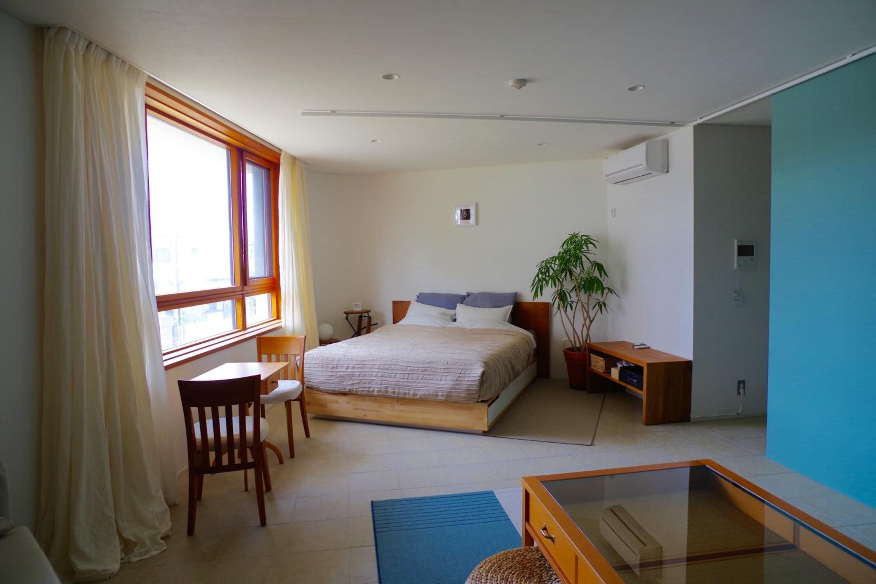A bedroom with a bed, a desk, a chair, a potted plant, and a window with curtains.