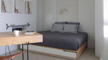 A bedroom with a bed, a desk, and a chair. There are three artworks on the wall, a bookshelf, and a window with curtains.