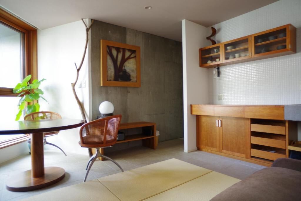 Ein moderner Essbereich mit einem runden Tisch, Stühlen und einer Pflanze. An der Wand hängt ein Gemälde und über der Arbeitsplatte befinden sich Holzschränke.