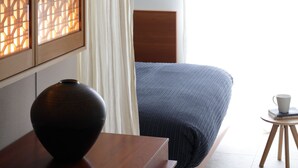 A bedroom with a bed, a wooden dresser, a vase, and a small table with a cup. - Sango Katase Guest Rooms (Fujisawa)