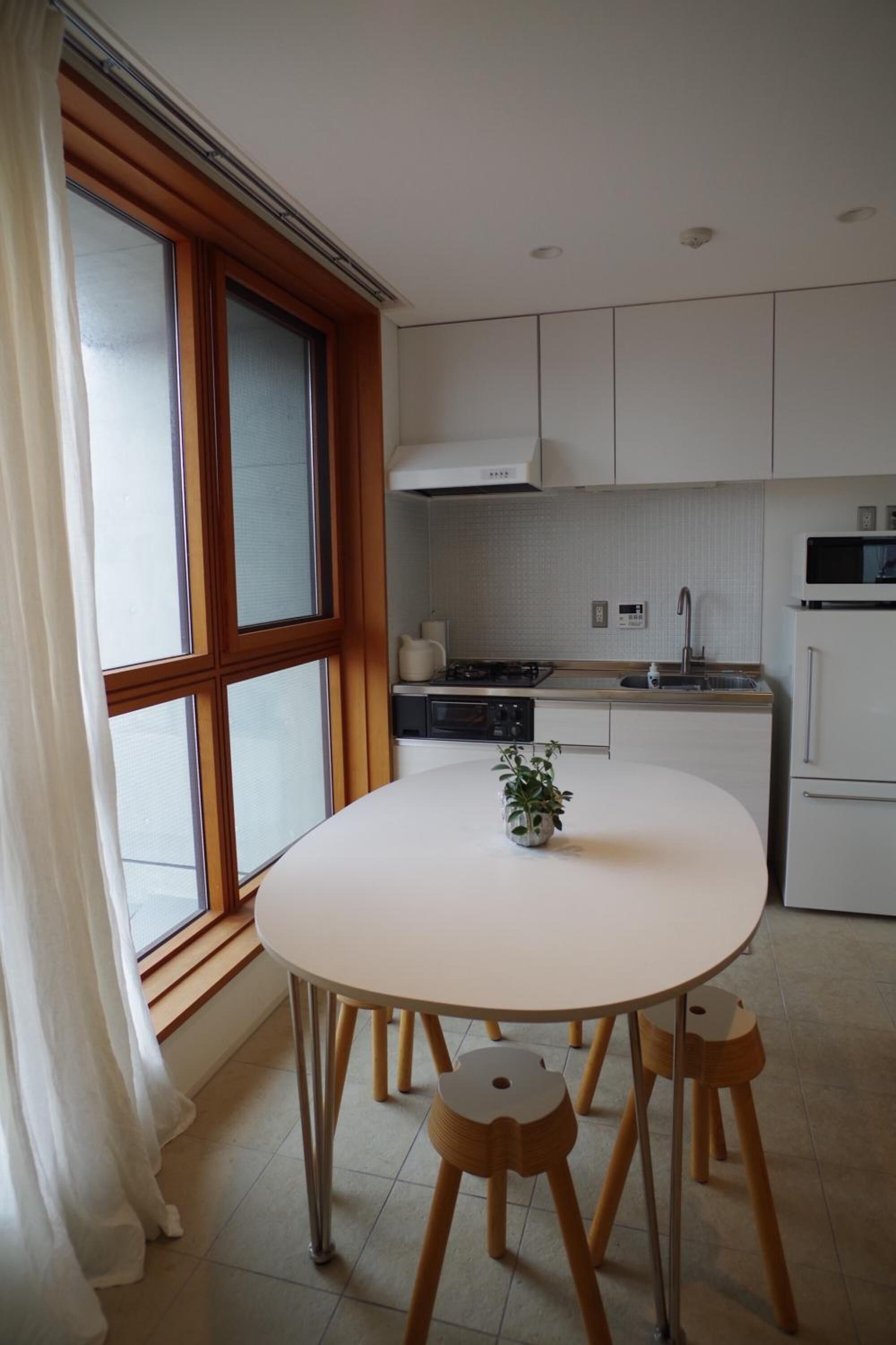 A modern kitchen with white cabinets, a round table with wooden stools, and a window with curtains.