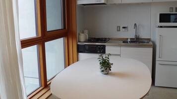 A modern kitchen with white cabinets, a round table with wooden stools, and a window with curtains.