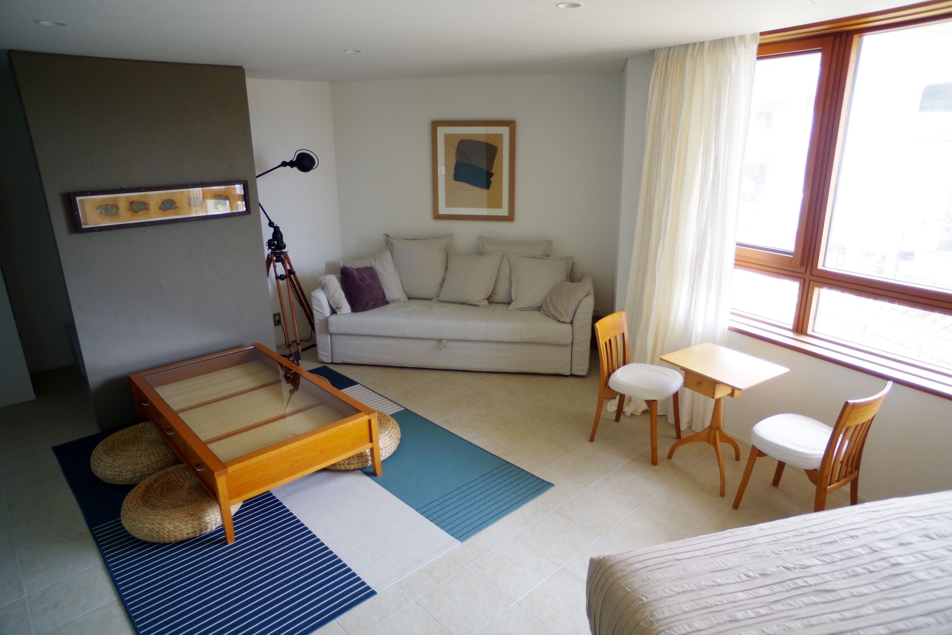 A room with a sofa, a small table with two chairs, a bed, and a lamp.