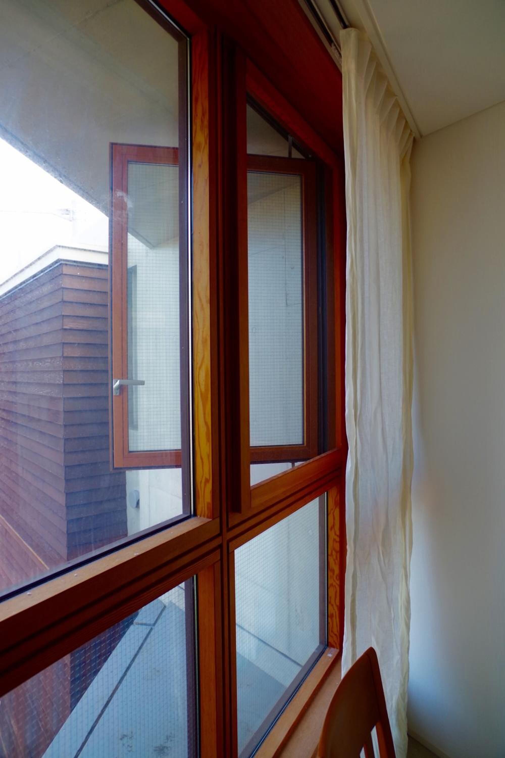 A room with a large window, a wooden chair, and a view of a building outside.
