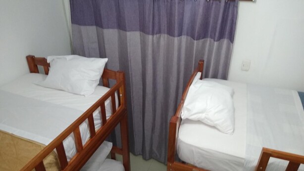 Two wooden bunk beds with white bedding in a room with a curtain. - Bachíg Hospedaje (Moyobamba)