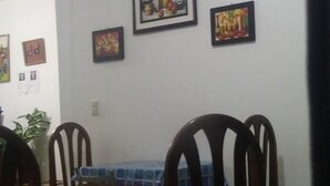 Un comedor con una mesa cubierta por un mantel azul a cuadros, rodeada de sillas de madera. En la pared sobre la mesa hay cuadros enmarcados.