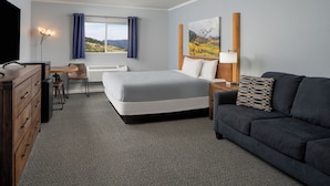 A hotel room with a bed, a desk, a chair, a sofa, a TV, and a window with curtains. - Gold King Mountain Inn (Cripple Creek)