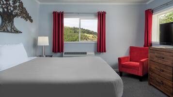 Ein Hotelzimmer mit einem großen Bett, einem roten Sessel, einer Holzkommode, einem Fernseher und einem Fenster mit roten Vorhängen.