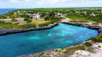 Uma área costeira com mar azul cristalino, uma pequena enseada e alguns edifícios dispersos.