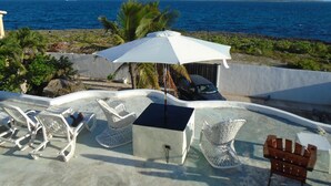 Terraço no topo com vista para o mar, com espreguiçadeiras, uma mesa e uma churrasqueira.