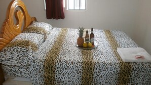Uma cama com colcha de onça, um bandeja com frutas e bebidas, e uma janela com cortinas.