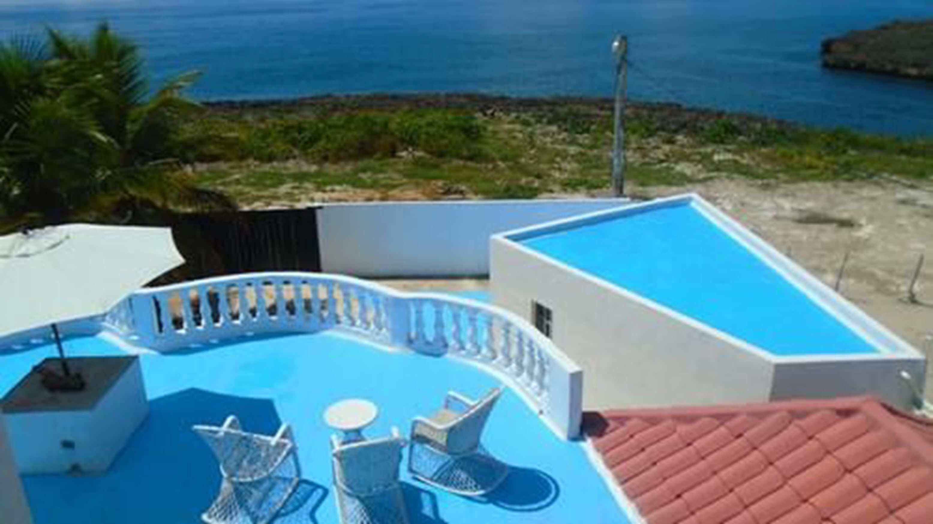 A rooftop pool with a view of the sea, surrounded by a white wall and a red roof.