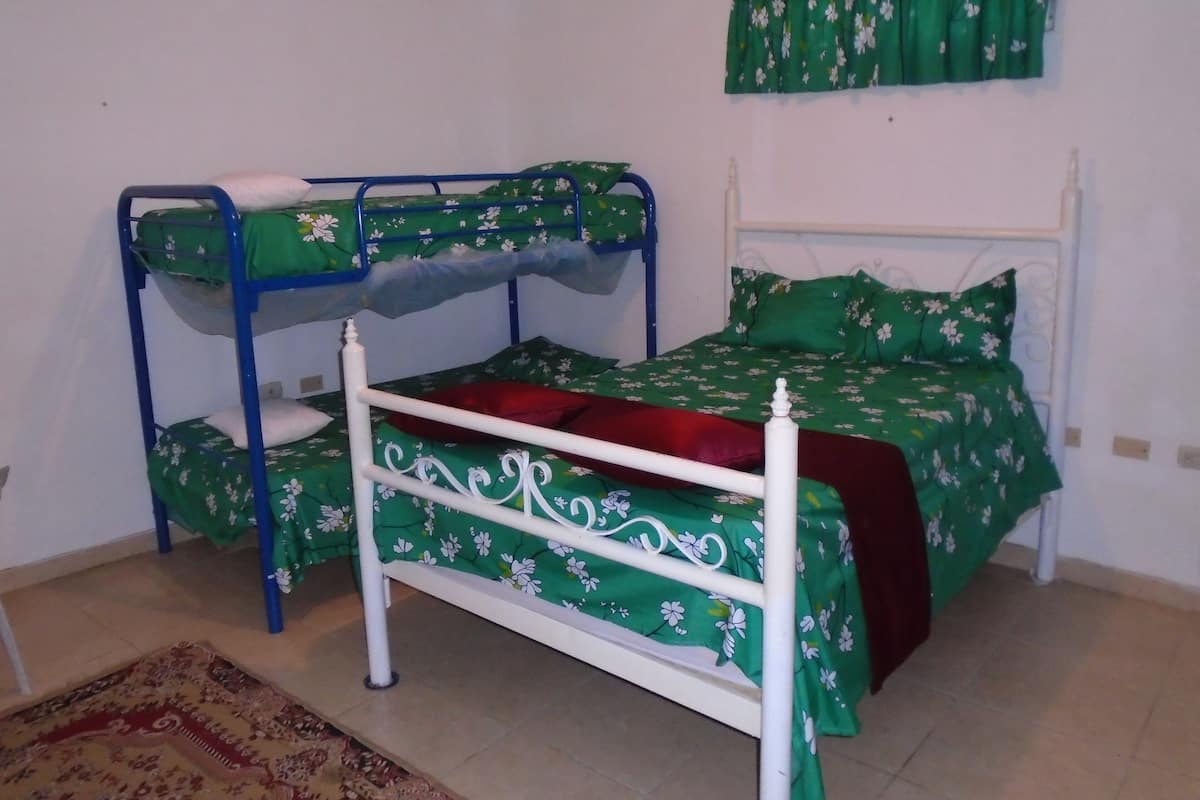 A bunk bed with green floral bedding, a white headboard, and a red pillow.