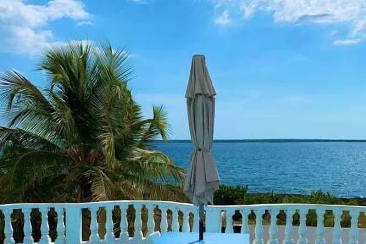 A poolside area with two wicker chairs and a table, a white railing, and a view of the ocean.