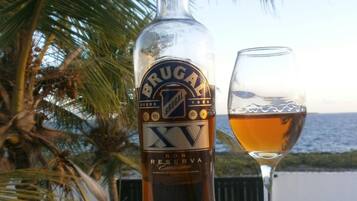 A bottle of Brugal Ron Reserva on a table with a glass of amber liquid beside it, set against a backdrop of palm trees and a view of the sea.