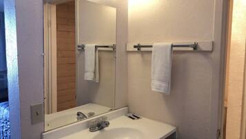 A bathroom with a white sink, a mirror, and two towels hanging on towel bars.