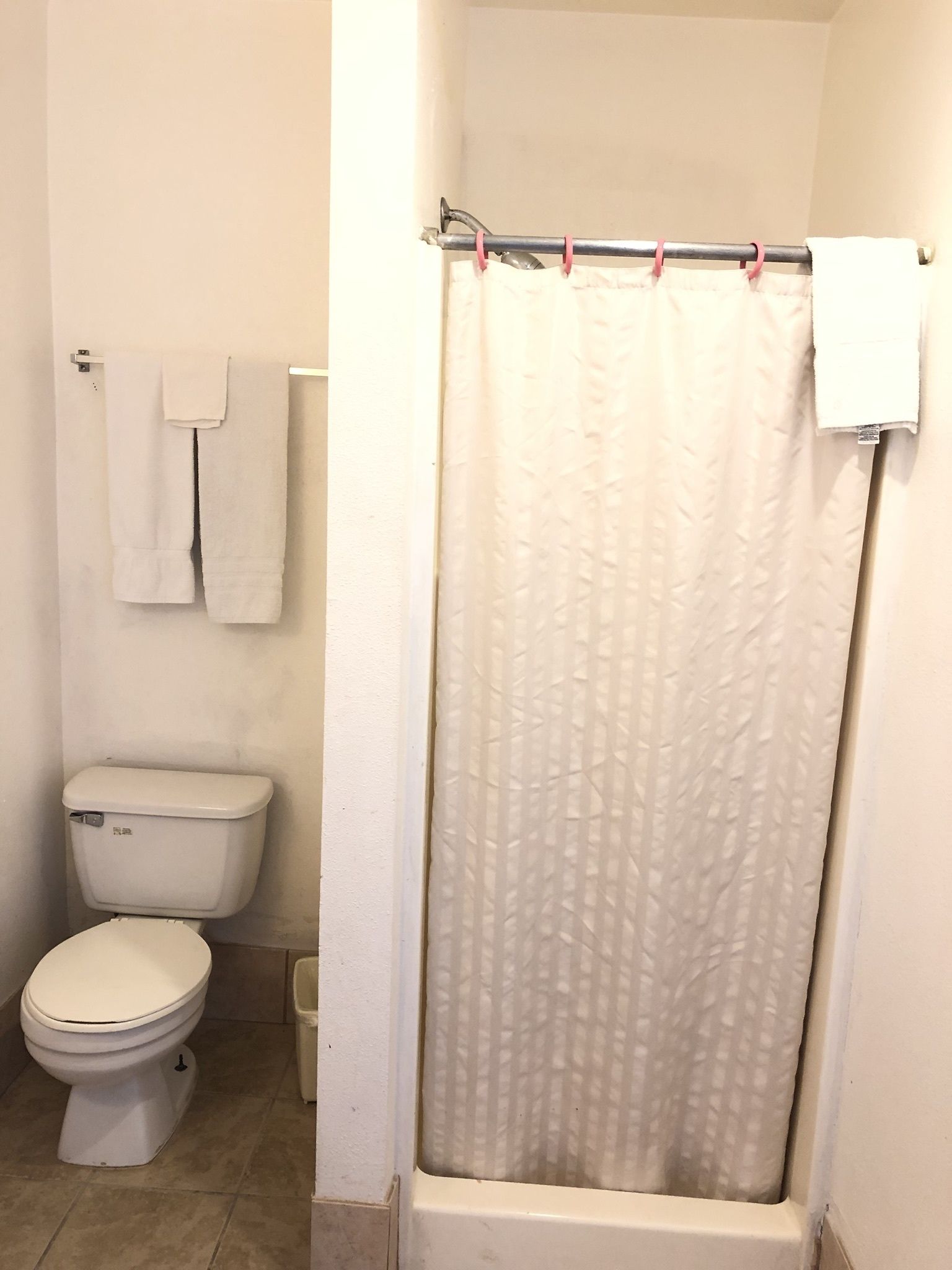 A bathroom with a toilet, a bathtub with a shower curtain, and a towel rack with two towels.