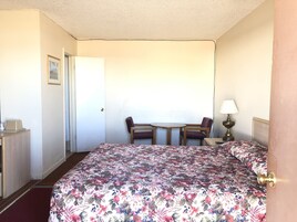 Una habitación de hotel con una cama, un escritorio, una silla, una mesita y una lámpara.