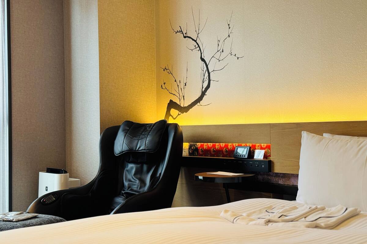 Ein Hotelzimmer mit Bett, Massagesessel, Schreibtisch mit Computer und Wandbild.