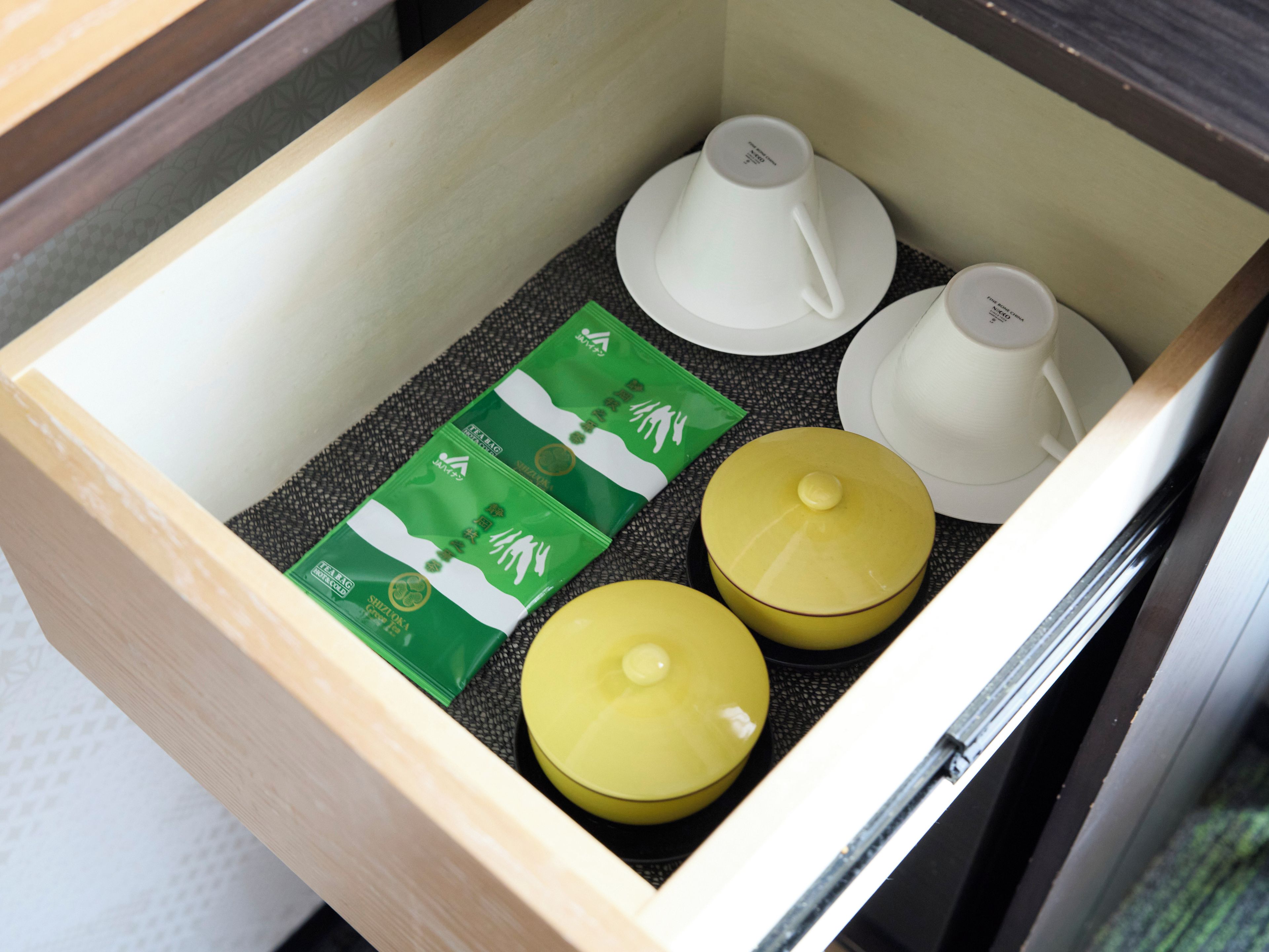 A drawer containing tea bags, a yellow container, and white cups.