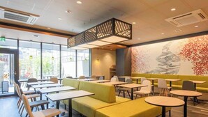 Un restaurante moderno con asientos tipo banca amarillos, mesas redondas y un mural grande en la pared.