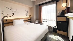 Habitación de hotel con una cama grande, un escritorio con silla, una mesita, un espejo y una ventana con cortinas.