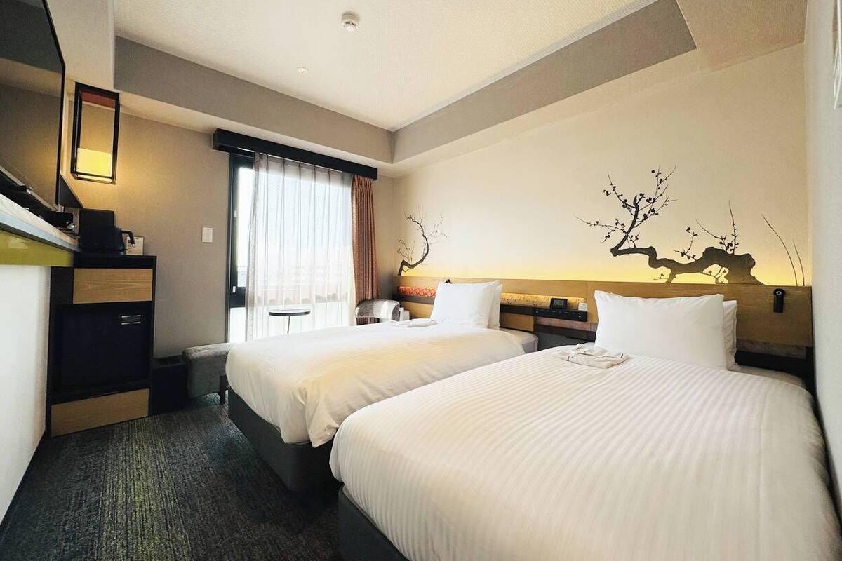 Ein Hotelzimmer mit zwei Betten, einem Schreibtisch, einem Stuhl, einer Lampe und einem Wandbild.